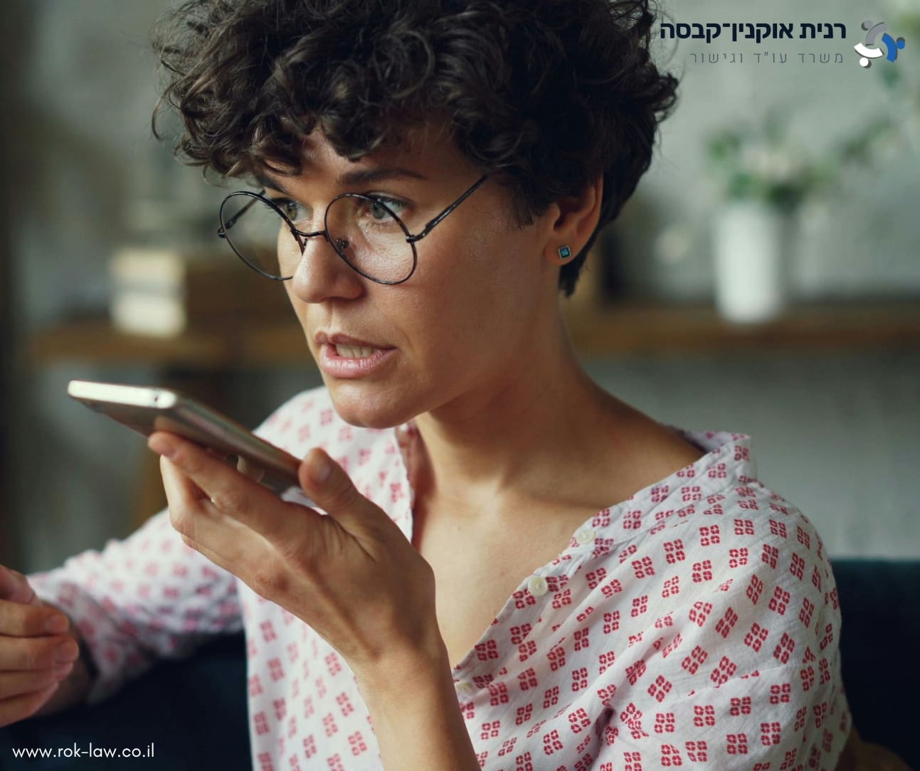 אישה עם משקפיים מקרבת טלפון אל פיה, מבט מרוכז וקשוב